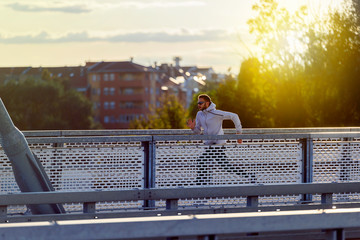 Fototapeta na wymiar Attractive fit man running fast along big modern bridge. Exercising, Jogging, Sport, Winter. Male athlete running.