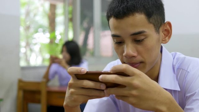 Asian high school students in a white uniform, who are a lot of addicted to games. They are playing exciting games on  their mobile phones and sitting in the classroom.