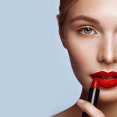Beautiful girl with red lips and classic makeup with lipstick in hand. Beauty face - obrazy, fototapety, plakaty