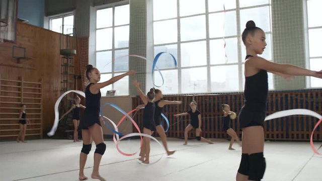 Group of athletic young teenage girls in sportswear rehearsing rhythmic gymnastics moves with ribbons