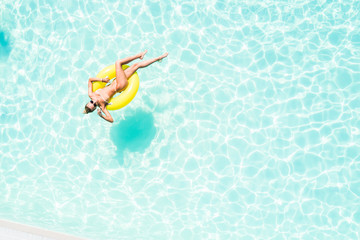 Beautiful young woman in swimming pool aerial top view from above. Girl in bikini relaxes and swims on inflatable ring has fun in water on family vacation