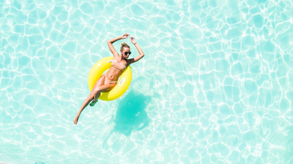 Beautiful young woman in swimming pool aerial top view from above. Girl in bikini relaxes and swims on inflatable ring has fun in water on family vacation