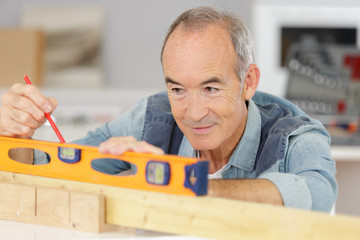 senior man measuring wall with construction level