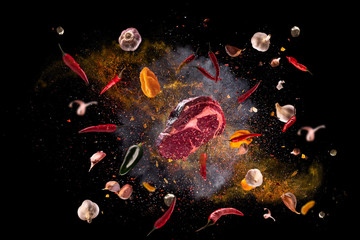 Hot red pepper, garlic, different spices powder meat stakes flying on a black background Motion...