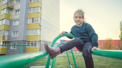 A charming little girl in casual clothes sits on a metal structure in the yard.