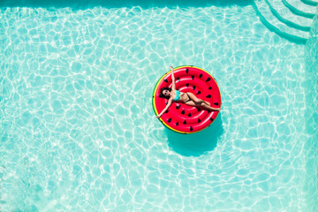 Aerial top of woman in bikini sitting in inflatable watermelon in pool