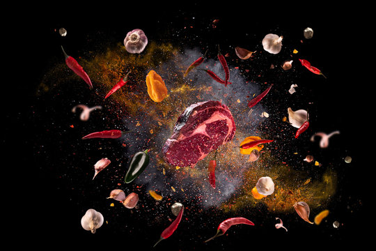 Hot red pepper, garlic, different spices powder meat stakes flying on a black background Motion freeze photo composition