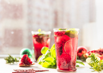 Fresh cold purple lemonade with mint, pomegranate, lime and ice in glass in the sun with shadow against blurred background. Festive drink. Christmas or New Year concept. 