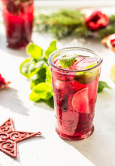 Fresh cold purple lemonade or cocktail with mint, pomegranate, lime and ice in glass in in the morning light, sunlight shadow. Christmas or New Year concept. Trendy style with artistic shadows.