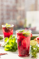 Fresh cold purple lemonade with mint, pomegranate, lime and ice in glass in the sun with shadow against blurred background. Festive drink. Christmas or New Year concept. 