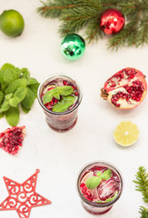 Cold purple cocktail or lemonade with fruit juice, lime slices, mint leaves, pomegranate and ice cubes on light grey background. Christmas or New Year concept.