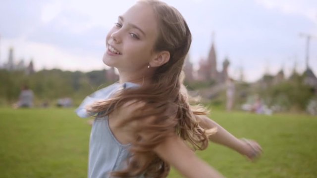Charming long-haired 10 years old girl in a blue dress circling in the dance in a city park, summer. Slow motion, close-up. Moscow Kremlin in defocus on the background. cloudy day