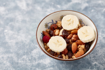 Bowl of granola with nuts, raisins and banana. Concept for a tasty and healthy meal. Rustic wooden background. Copy space. 