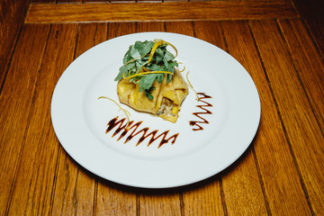 appetizing pancake with stuffing. Arugula. On a white plate on a wooden table