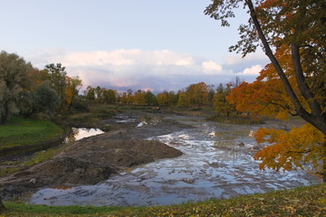 The river flows along the bottom of a pond drained for restoration in the park. Awesome autumn background.