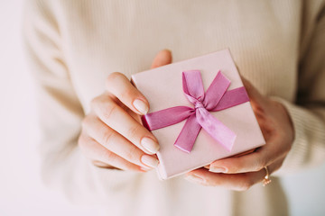 Closeup image of female hands, holding present with pink ribbon. Festive backdrop for holidays: Christmas, New Year, Valentines day, Birthday, .