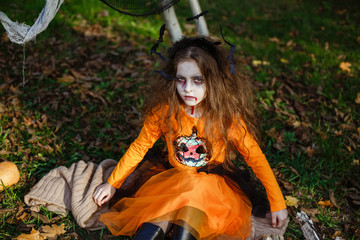Portrait of masked little girl in zombies, wearing Halloween orange costume. Children's party.