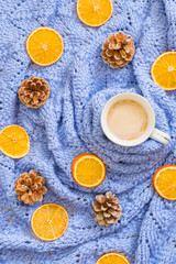 Fototapeta na wymiar Winter mood composition. Cup of coffee, knitted blue blanket, dry oranges, pine cones. Flat lay, top view