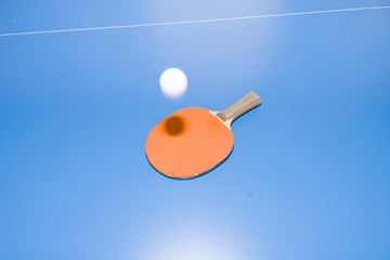 white ping pong ball hovering over a table tennis racket lying on a table