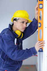 smiling woman builder in hardhat doing measures with level tool