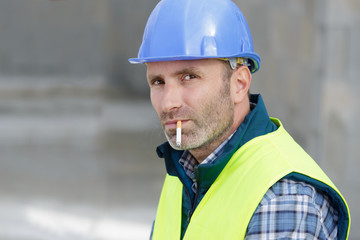 male worker wearing a refective vest smoking a cigarette