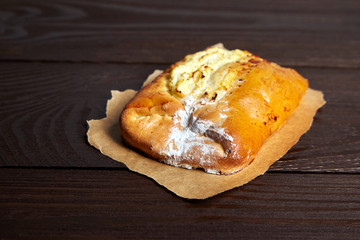 Wheat bun with curd filling on a wooden table, close-up. Bakery, bun with cottage cheese on baking paper on brown background
