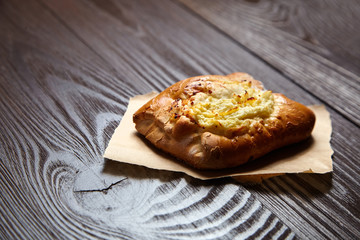 Wheat bun with curd filling on a wooden table, close-up. Bakery, bun with cottage cheese on baking paper on brown background