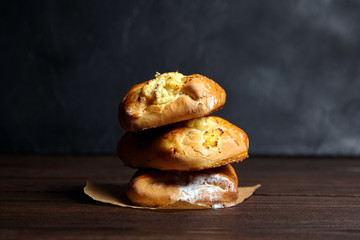 Wheat buns with curd filling on a wooden table, close-up. Bakery, three buns with cottage cheese stacked on baking paper on dark background