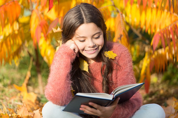 Her hobby is reading. Cute small child reading book on autumn day. Adorable little girl enjoy...