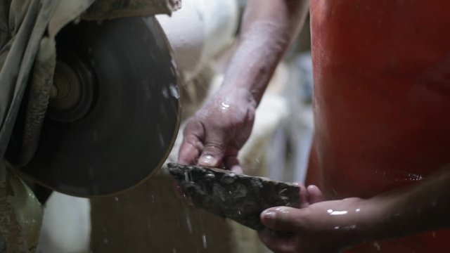 Slow motion shot of man working with semiprecious stone. Close up of hands slicing stromatolite rock fossil to creat jewelry with cutting disc and water. La Toma, San Luis, Argentina