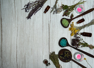 Aromatherapy and SPA care. The border is made of bunches of dried herbs, multi-colored sea salt, bottles with essential oils, candles and fragrant sticks on a white wooden background.