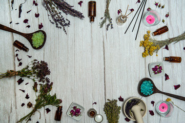 Aromatherapy and SPA care. The frame is made of bunches of dried herbs, colorful sea salt, small bottles of essential oils, candles and incense on a white wooden background.