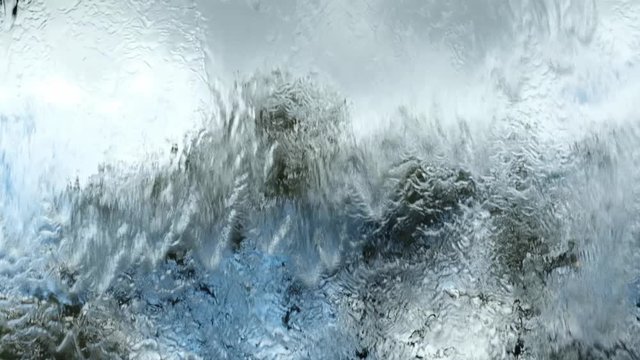Blurreed silhouettes of trees behind glass wall with flowing water in slow motion