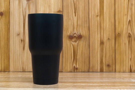 Black colour stainless steel tumbler or cold and hot storage cup on wood.