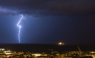 Massive cloud to ground lightning bolts hitting the horizon of city lights