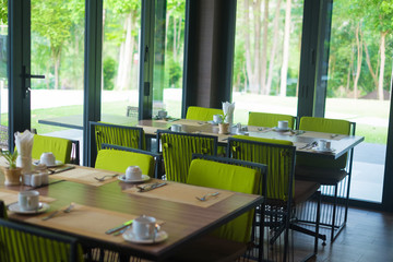 Empty restaurant part of hotel with table and armchair near windows and garden view.