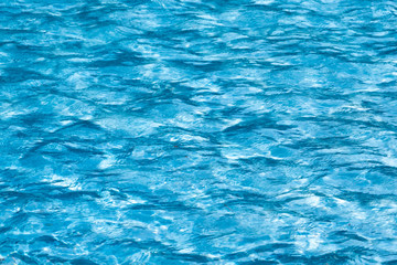 Blue and bright ripple water surface in swimming pool with sun reflection.