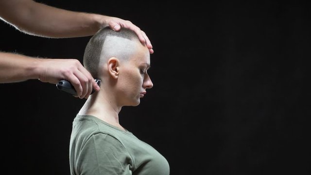 concept military girl. hands of a man hairdresser shave a woman's head bald, army hairstyle. Black background