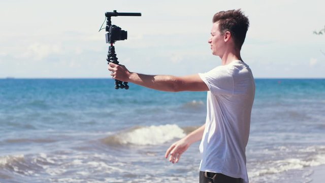 Young male vlogger filming travel story on the beach.