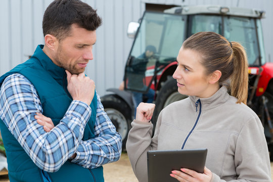 Male And Female Farmers Talking Next To A Tractor