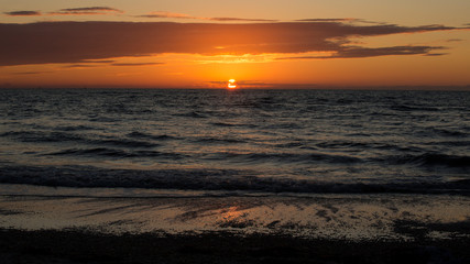 Naklejka premium Orange sun highlights storm clouds on a warm evening on a Gulf Coast Florida beach.