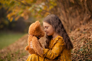 portrait of a happy cute girl of 8-9 years old in autumn park with a toy bear cub in her hands