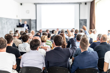 I have a question. Group of business people sitting at the chairs in conference hall. Businessman...