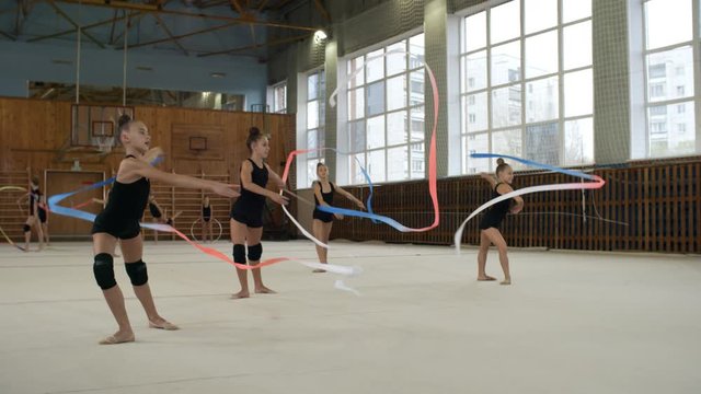 Group of teenage girls in sports clothes rehearsing rhythmic gymnastics dance and using ribbons
