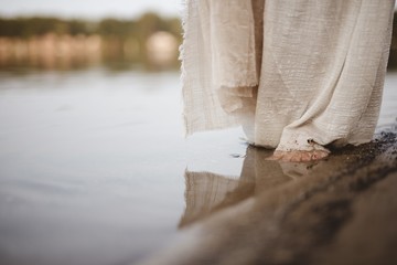 Closeup shot of a person wearing a biblical robe walking on the shoreline
