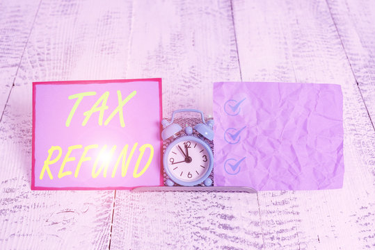 Text sign showing Tax Refund. Business photo text refund on tax when the tax liability is less than the tax paid Mini blue alarm clock standing above buffer wire between two notation paper
