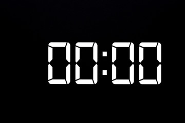Showing time 00:00 on white led digital clock isolated black background