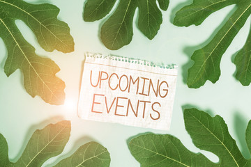 Writing note showing Upcoming Events. Business concept for the approaching planned public or social occasions Leaves surrounding notepaper above empty soft pastel table