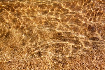 Golden sand under clear sea water and sunlight glow reflection close up top view, yellow sandy beach coast texture below transparent ocean surface background, abstract natural seaside pattern backdrop