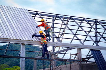 Roofer worker in protective uniform wear and gloves, using air or pneumatic nail gun and installing asphalt shingle on top of the new roof,Concept of residential building under construction. - obrazy, fototapety, plakaty